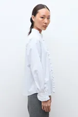 Camisa blanca de manga larga con cuello alto y volados en el cuello y puños.