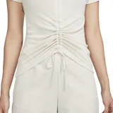 Remera blanca de algodón con cuello redondo, mangas cortas y ajuste ceñido. Presenta un cordón ajustable en el frente para crear un efecto fruncido. Logo de Nike bordado en el pecho.