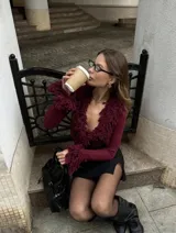 Buzo de punto bordó con escote en V pronunciado, mangas largas y detalles de flecos texturizados en el cuello y los puños.