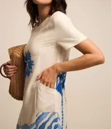 Vestido corto tipo t-shirt color crudo, con estampado de palmeras y olas en tonos azules.