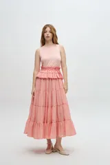 Vestido largo color salmón, con cuerpo ajustado de algodón y falda amplia de rayon, nylon, poliéster y elastano. Presenta un volante plisado en diagonal desde el hombro hasta la cintura.