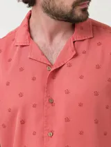 Camisa de manga corta color salmón con estampado de motivos florales, cuello cubano y cierre frontal con botones.