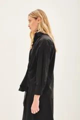 Camisa de popelina de algodón en color negro, con corte amplio, cuello clásico y cierre frontal con botones. Presenta un diseño versátil con botones en los laterales que permiten un ajuste cruzado.