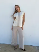 Top sin mangas tejido en hilo color crema, con cuello redondo y rayas verticales grises. Presenta un logo bordado en el pecho.