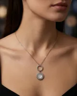 Collar de cadena fina de acero con dije colgante compuesto por dos círculos entrelazados, uno de acero liso y otro con incrustación de nácar en el centro.