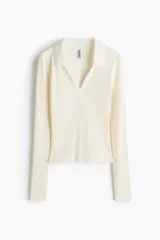 Top entallado corto de punto acanalado color blanco crema, con cuello camisero y escote en V. Tiene mangas largas.