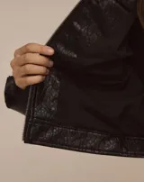 Chaqueta de efecto cuero texturizado en color negro, con corte cropped y silueta estructurada. Presenta cierre frontal con cremallera, bolsillos delanteros con cierre y cremalleras en los puños.