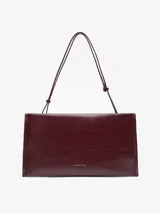 Bolso tipo clutch de Adolfo Dominguez en color bordó con acabado brillante y textura craquelada. Cuenta con un compartimento principal con cierre magnético, bolsillo interior con cremallera, asa de mano integrada y asa larga regulable y extraíble.