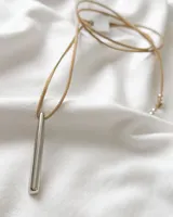 Gargantilla con tiento de cuero color beige y dije plateado en forma de barra.