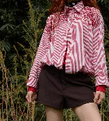 Camisa oversize de corte recto con estampado de rayas verticales blancas y negras. Presenta un diseño distintivo con bordados artesanales de mostacillas y lentejuelas negras en la zona de los hombros y el pecho, cuello clásico y cierre frontal con botones.
