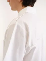 Camisa blanca de manga corta, con cuello clásico, cierre frontal con botones y un bolsillo aplicado en el pecho.