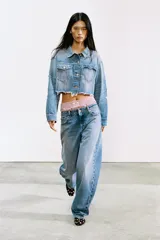 Cazadora crop de denim celeste desgastado, con cuello solapa, manga larga y bajo deshilachado. Presenta parches en forma de corazón en los bolsillos delanteros y detalles de roturas.