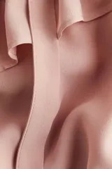 Blusa rosada de manga larga con cuello alto y lazo para atar. Presenta ribetes de volados que cruzan el pecho y puños con elástico fruncido.