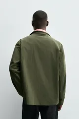 Parka de hombre color verde militar, corte regular, confeccionada en tejido técnico ligero. Presenta cuello subido, manga larga con puño ajustable y cuatro bolsillos frontales de plastrón con solapa. Cierre frontal con cremallera.