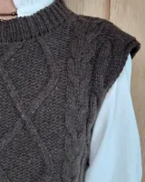 Chaleco de punto gris oscuro con diseño de trenzas y rombos en relieve, cuello redondo y terminaciones acanaladas.