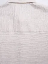 Camisa de manga corta color blanco con textura tipo waffle, cuello clásico, cierre frontal con botones de madera, bolsillo de parche en el pecho y parche con logo en el ruedo.