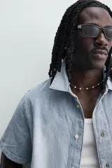 Camisa de corte boxy fit confeccionada en denim ligero de algodón. Presenta cuello solapa, manga corta y cierre frontal con botones. Diseño con efecto lavado.