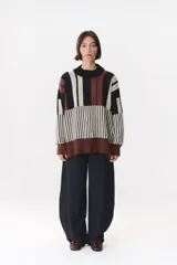 Buzo de tejido de punto con diseño de bloques de rayas verticales en colores rojo, verde, bordó y crema. Presenta cuello alto, corte oversize y terminaciones en rib en puños y ruedo.