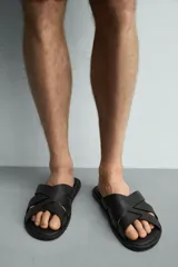 Sandalia plana de hombre confeccionada en piel color negro, con diseño de tiras cruzadas y entrelazadas en el empeine.