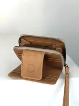 Billetera pequeña de cuero color marrón claro con paneles frontales de pelo natural. Presenta un cierre de solapa con broche y un logo grabado de un búho. Incluye una correa de muñeca extraíble.
