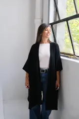Poncho abierto de tejido de punto color negro, con mangas tres cuartos y bolsillos laterales.