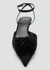 Zapato tipo kitten heel color negro, con punta fina y detalle de pompones en el empeine. Cuenta con una tira ajustable con hebilla en el tobillo.