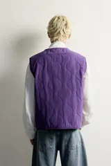 Chaleco acolchado de algodón color violeta con efecto lavado, cuello en V, cierre frontal con cremallera y bolsillos de plastrón delanteros.