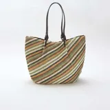 Bolso tipo capazo grande de tejido trenzado con diseño de rayas diagonales multicolor en tonos verdes, marrones, blancos y negros. Cuenta con doble asa de hombro en cuero sintético marrón.