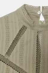 Camisa verde claro con cuello alto de puntilla, manga larga y detalles de entredoses calados en el pecho y los hombros. Cierre en la espalda con abertura y botón oculto.