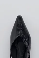 Zapato tipo flat destalonado de color negro con acabado brillante, punta fina y cierre con hebilla lateral.