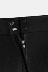Pantalón balloon de tiro alto color negro, con diseño de pierna ancha, trabillas en la cintura, pespuntes marcados a tono y cierre frontal con cremallera, botón y ganchos metálicos.