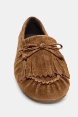 Mocasín plano confeccionado en serraje, con detalle de flecos y lazo decorativo en la parte delantera. Presenta pasadores laterales y acabado en punta redonda.