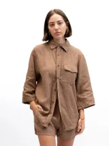 Camisa de lino color marrón, con cuello clásico, cierre frontal de botones, mangas tres cuartos y un bolsillo frontal en el pecho.