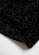 Blusa asimétrica de terciopelo negro con textura de flores en relieve, diseño de un solo hombro con manga larga y detalle de lazo con flor en el cuello.