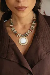 Collar corto con cadena compuesta por bastones de piedras naturales en tonos tierra y verdes, con un medallón central circular de nácar engarzado en metal plateado.