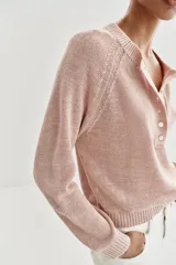Sweater de punto color beige con cuello redondo, manga larga y cierre frontal parcial con botones. Presenta terminaciones en rib en cuello, puños y dobladillo.