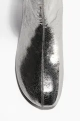 Botines de caña corta con acabado metalizado plateado y textura arrugada. Presentan punta redondeada, taco cuadrado revestido y cierre lateral oculto. El forro y las plantillas son de satén.