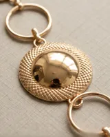 Cinto de metal dorado con diseño de eslabones circulares y apliques esféricos texturados.