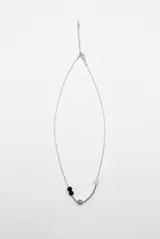 Collar de metal plateado con cadena fina, detalles de cuentas esféricas de colores azul oscuro, gris y blanco, y una barra curva decorativa.