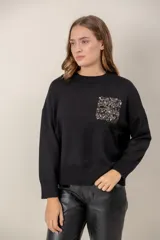Sweater negro de punto con cuello redondo, mangas largas y un bolsillo frontal decorado con lentejuelas brillantes.
