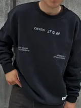 Buzo negro de corte holgado con cuello redondo y puños acanalados. Estampado frontal con la palabra "OSTEN" y la frase "NOT WHERE YOU'RE FROM A MINDSET OF BECOMING" en color blanco.