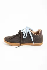 Zapatilla de cuero marrón oscuro, estilo deportivo retro, con suela de goma color caramelo. Presenta costuras decorativas en el cuerpo y el nombre "LEMON" grabado en dorado en el lateral. Se muestra con dos cordones anudados: uno celeste claro y otro marrón oscuro.