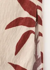 Vestido midi entallado de diseño asimétrico con un solo hombro y una manga larga, confeccionado en color beige con estampado de hojas en tonos bordó. Presenta un cuerpo fruncido y detalle drapeado.