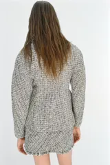 Chaqueta cruzada de estructura en tejido tweed de mezcla de hilos en tonos blanco y negro, con escote en pico, manga larga y cierre frontal con botones a presión ocultos.