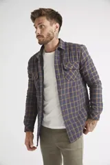 Sobrecamisa de viyela para hombre con estampado de cuadros en rojo y negro. Presenta cierre frontal con botones, bolsillos en el pecho con solapa y botón, y un interior capitoneado para mayor abrigo. Cuenta con un logo en grifa de cuero.