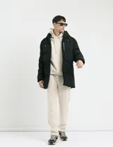 Campera puffer de corte largo, color verde militar, con capucha fija, cierre frontal y puños elásticos internos.