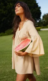 Vestido corto color beige, de lino y corte en A, con escote en V con tiras para anudar y mangas amplias.