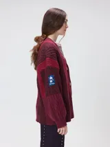 Cardigan oversize de tejido de punto grueso con diseño de bloques de color en tonos tierra. Presenta cuello en V, cierre frontal con botones, mangas largas con terminación abullonada y parches decorativos en el pecho y hombro.