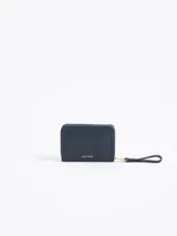 Billetera compacta de cuero vacuno color bordó, con cierre perimetral, correa de muñeca y aplique metálico dorado en forma de mariquita en el frente.