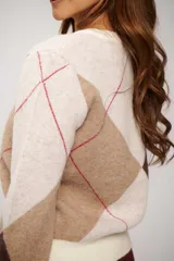 Buzo de tejido de punto con escote en V y diseño de rombos en tonos crudo, marrón y beige, con detalles de líneas finas en color rojo.